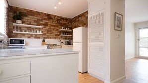 Una cocina moderna con armarios blancos, una pared de ladrillo decorativa y estantes empotrados.