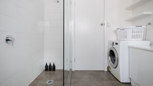 Un baño moderno con cabina de ducha de vidrio, una puerta blanca, una lavadora y una cesta de ropa.