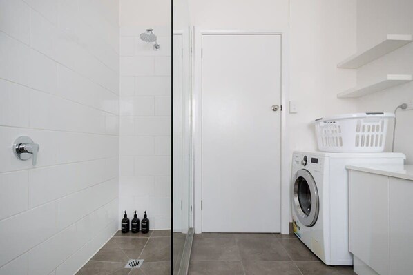 Un baño moderno con cabina de ducha de vidrio, una puerta blanca, una lavadora y una cesta de ropa.