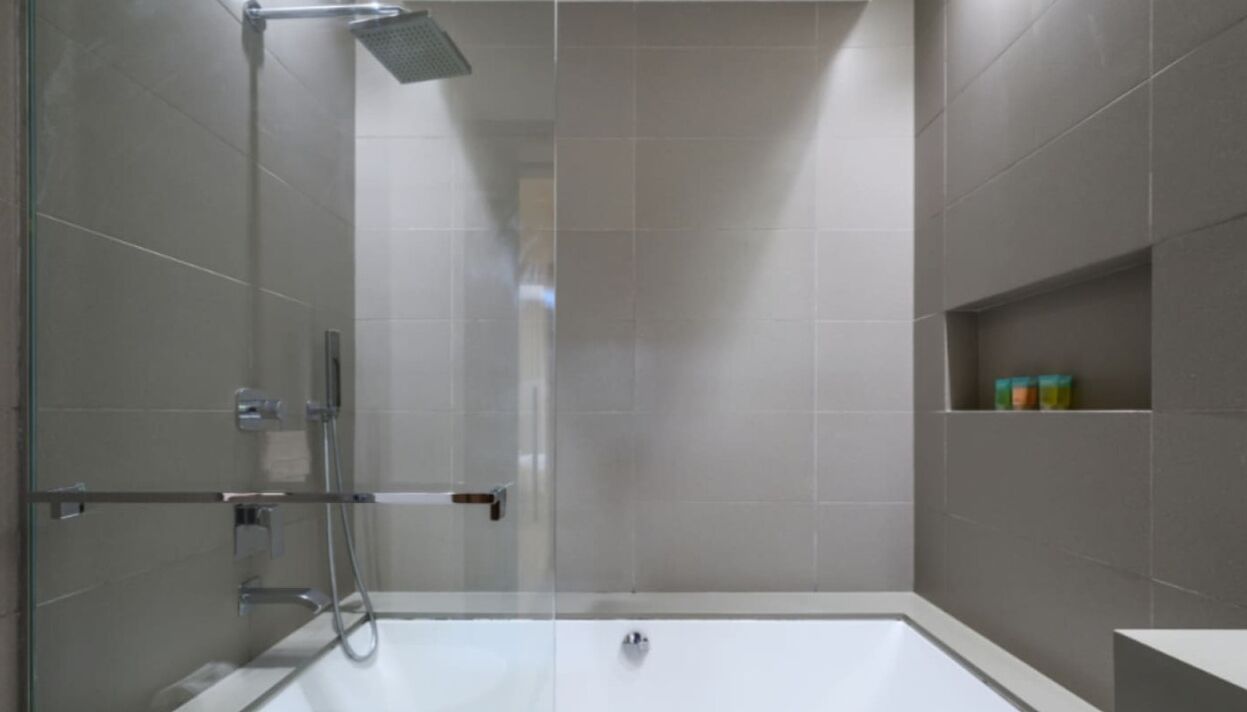 Une douche moderne dotée d’une porte en verre, d’un pommeau de douche à main et d’un panneau de commande fixé au mur.