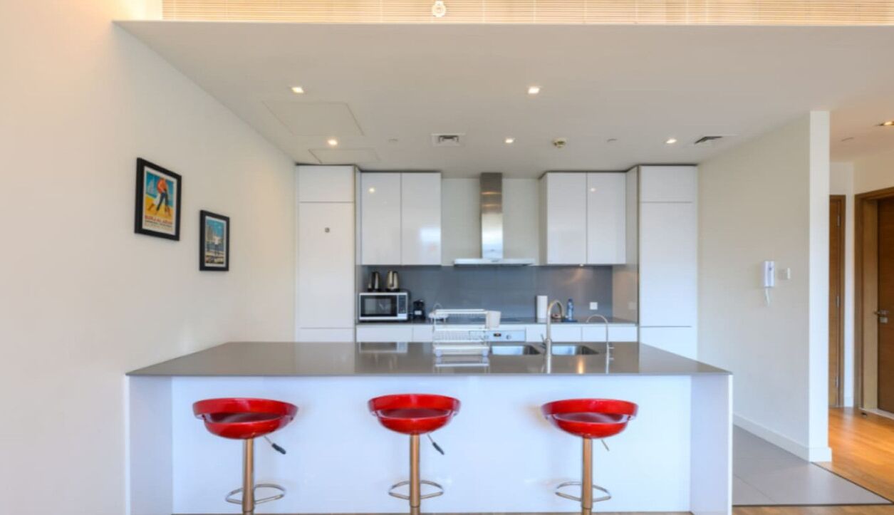 Une cuisine moderne avec des meubles blancs, un îlot central doté de tabourets de bar rouges et un four à micro-ondes.