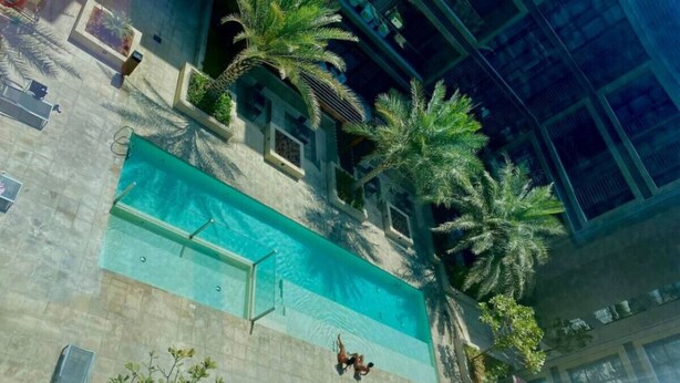 Una piscina interior con agua cristalina, rodeada de palmeras y un muro de piedra.