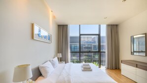 Habitación de hotel con una cama grande, una ventana con cortinas, una mesita de noche con lámpara y un cuadro enmarcado en la pared.