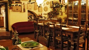A dining area with wooden tables and chairs, a red sofa, and a wine rack with bottles. - Apartment in Farmhouse with Swimming Pool in the Tuscan countryside of Cortona (cortona)