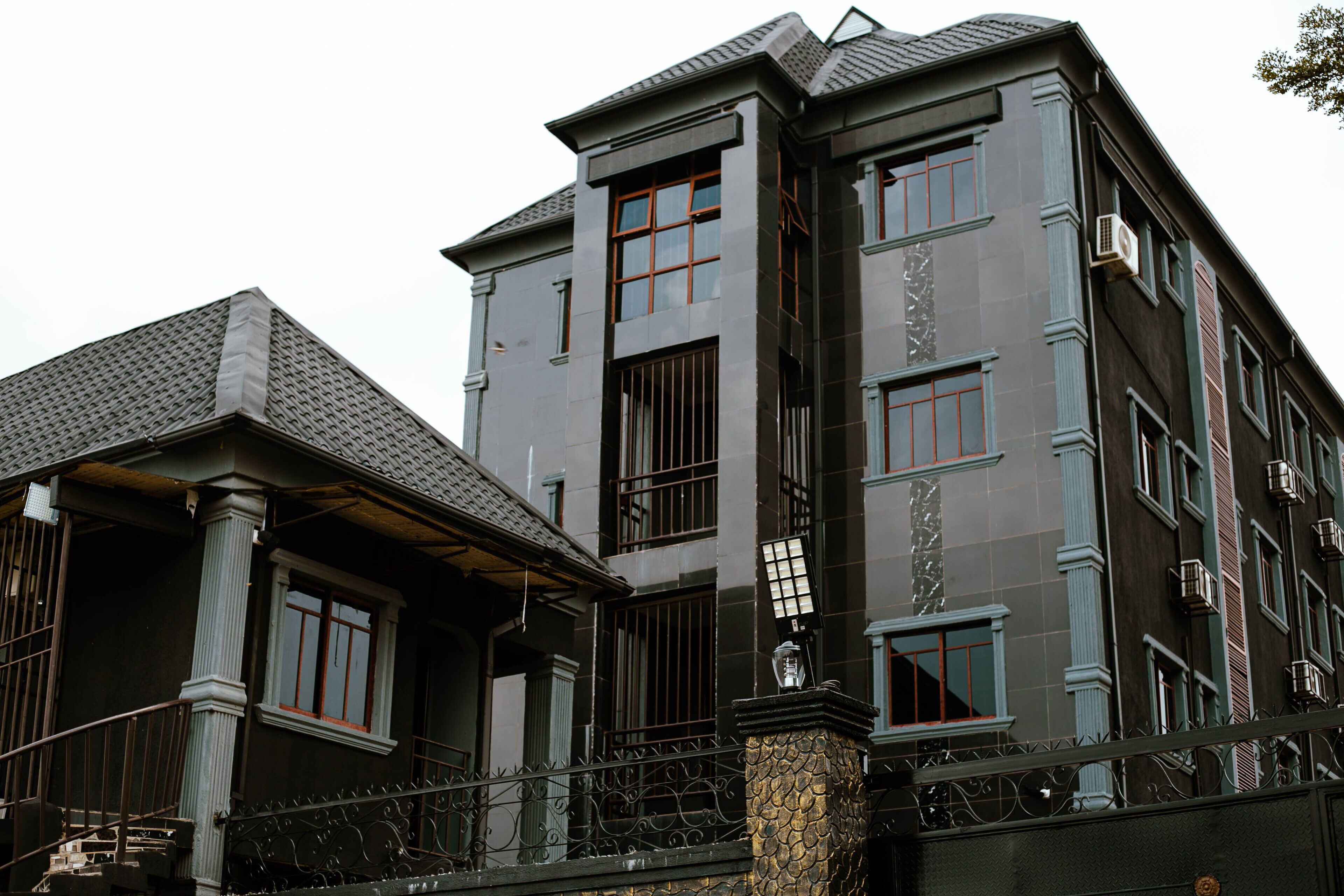 A multi-story building with a dark facade, large windows, and a balcony with ornate metal railings.