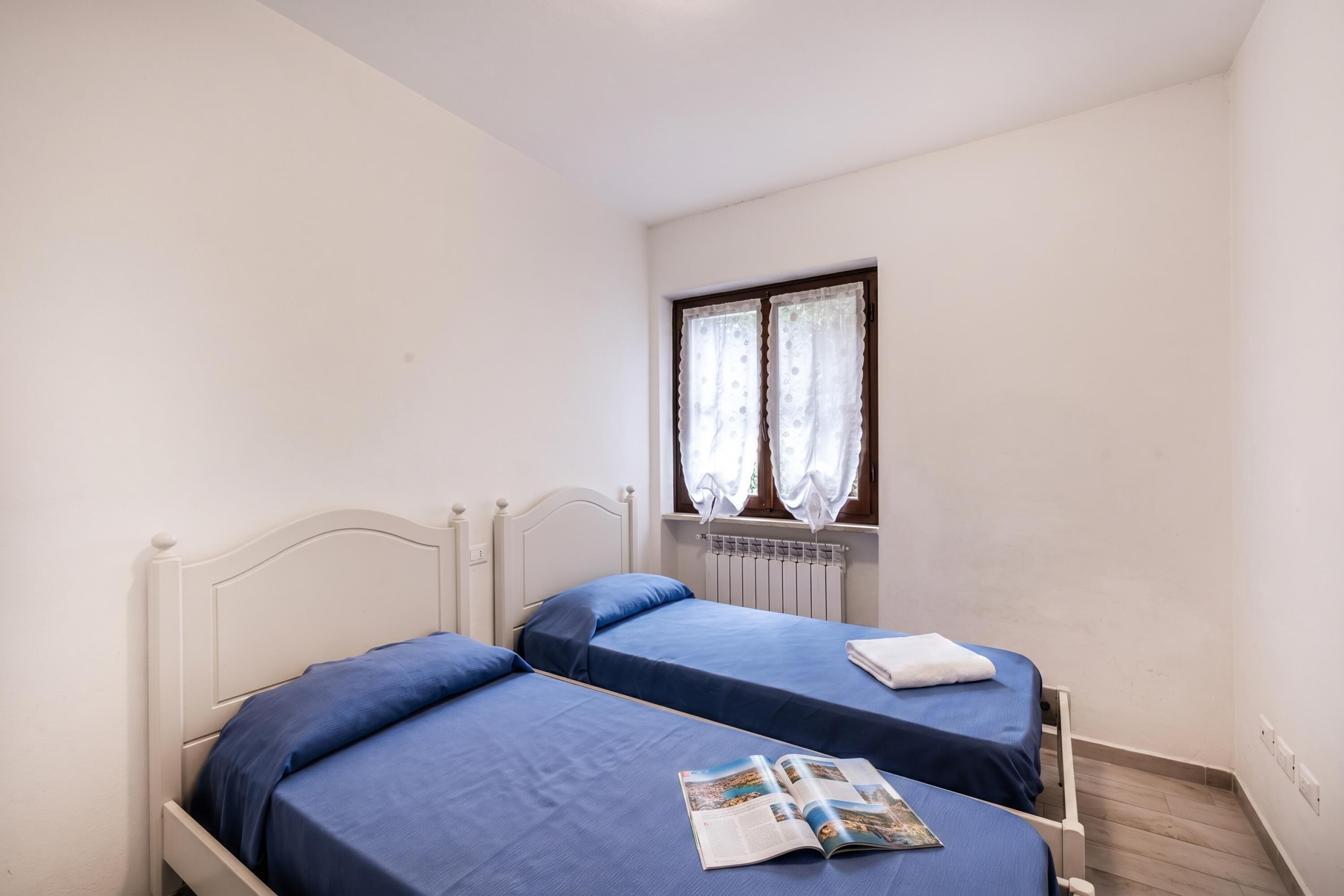 A room with two beds, a window with curtains, and a radiator.