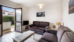 Una sala de estar moderna con un sofá, una mesa de centro y un televisor. Hay una puerta corrediza de vidrio que da a un área exterior.