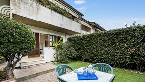 Un patio con una mesa y sillas, un pequeño jardín y un edificio con un balcón.