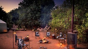 An outdoor camping area with a fire pit, lanterns, and chairs arranged around it. - Nkula Walking Camp by RETURN Africa (Mutale)