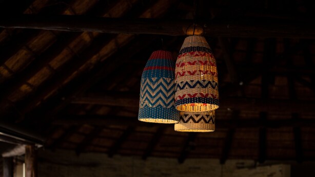 A cozy living room with a sectional sofa, patterned cushions, and hanging lamps. - Nkula Walking Camp by RETURN Africa (Mutale)