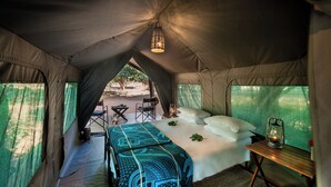 A tent with a bed, a table, and a lantern. - Nkula Walking Camp by RETURN Africa (Mutale)