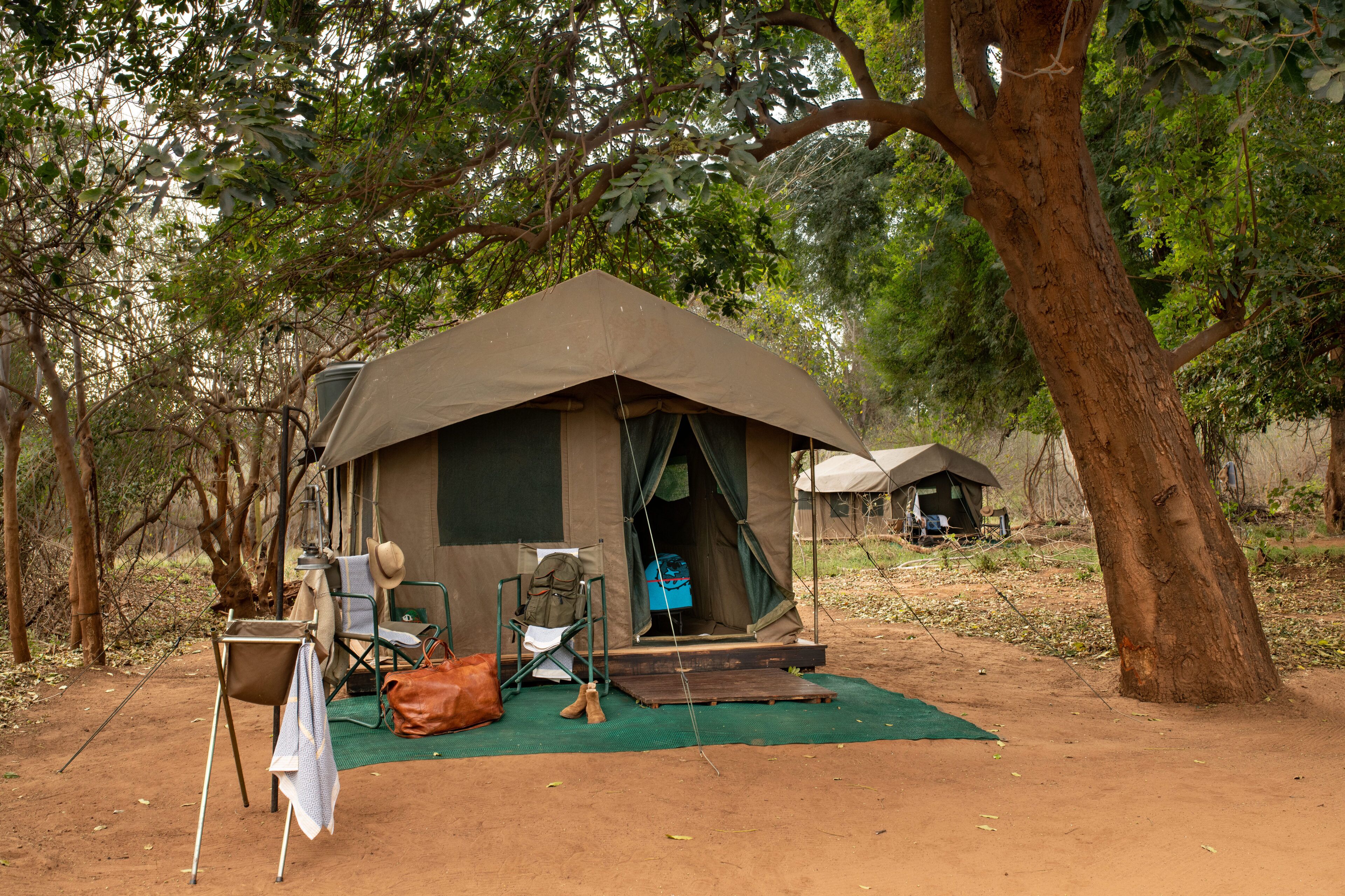 A tent with a chair and a table outside, surrounded by trees.
