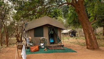 A tent with a chair and a table outside, surrounded by trees.