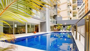 A modern indoor swimming pool with clear blue water, surrounded by glass walls and balconies.