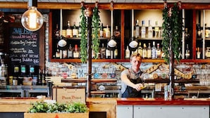 A bar with a wooden counter, shelves of liquor bottles, and a chalkboard menu listing drinks.