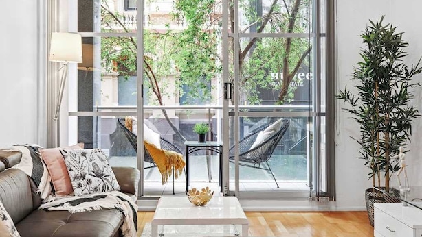 A modern living room with a leather sofa, a white coffee table, and a large window with a view of trees and buildings.