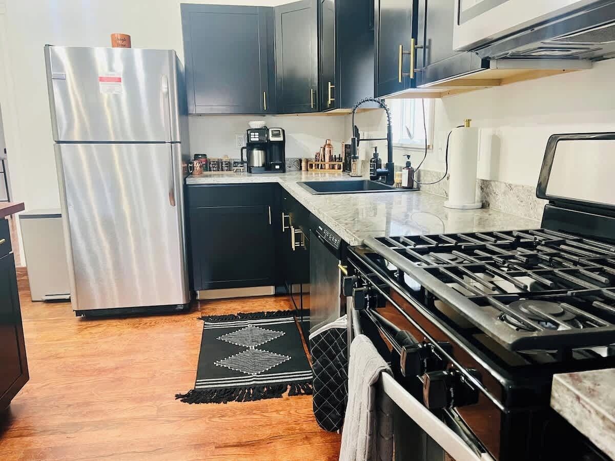 A kitchen with a stainless steel refrigerator, black cabinets, a gas stove, and a coffee maker.