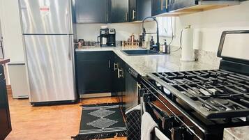 A kitchen with a stainless steel refrigerator, black cabinets, a gas stove, and a coffee maker.