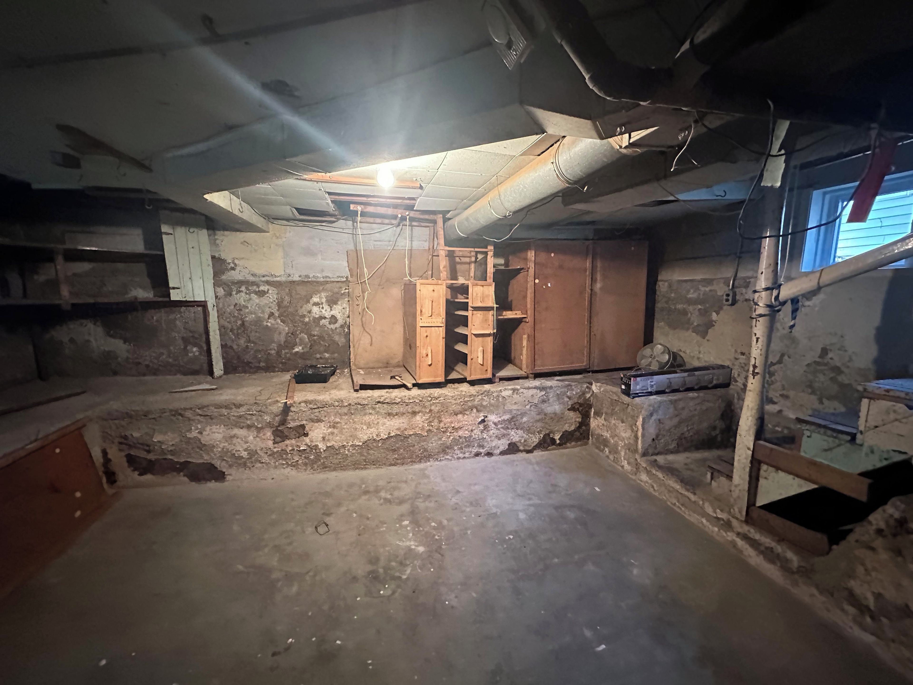 A basement with a wooden ladder, a fan, and a concrete floor.