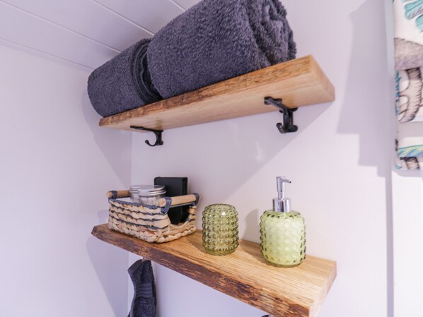 A wooden shelf with a rolled towel, a woven basket, and two glass bottles.