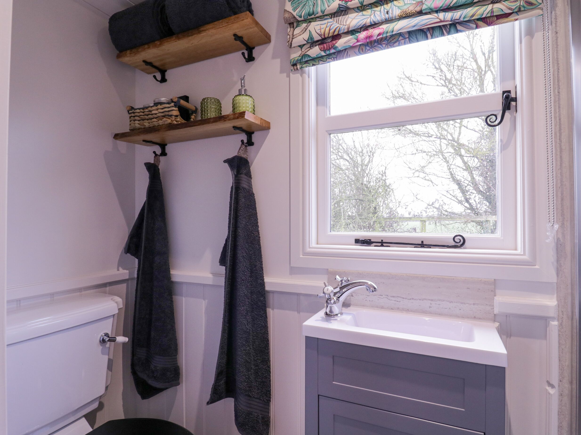 A bathroom with a white sink, a toilet, and two towels hanging on hooks. There is a window with a view of trees outside.