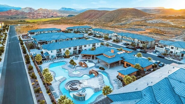 Un complex turístic amb diversos edificis, una piscina i un paisatge de muntanyes al fons.