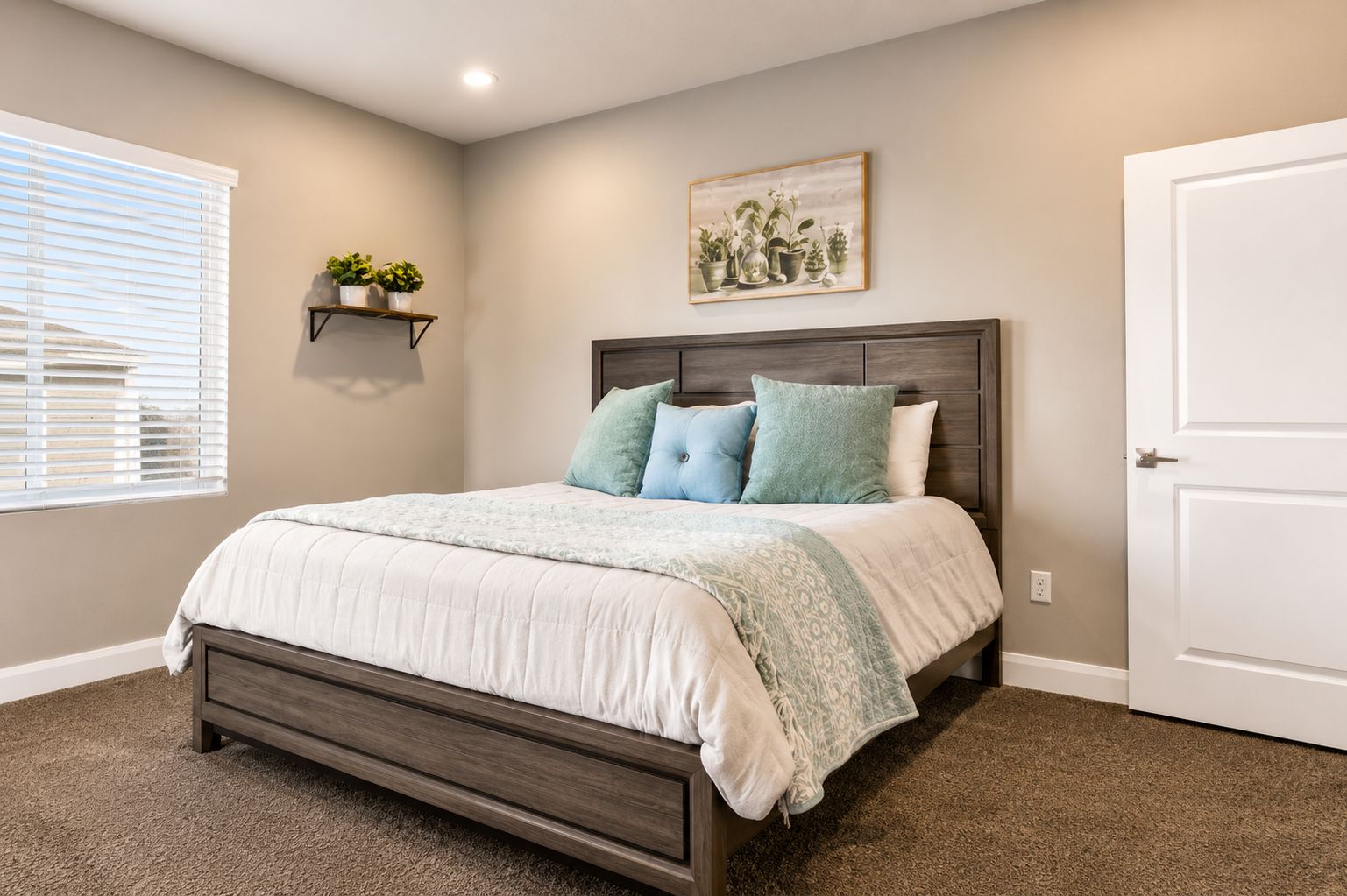 A bedroom with a bed, a headboard, a wall-mounted shelf with plants, a door, and a window with blinds.
