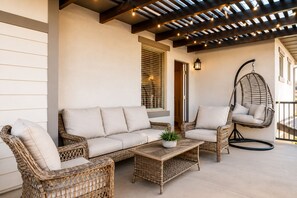 A covered outdoor seating area with wicker furniture, a hanging chair, and a potted plant.
