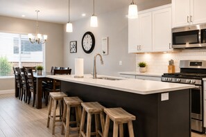 A modern kitchen with a central island, bar stools, a stainless steel stove, and a microwave.