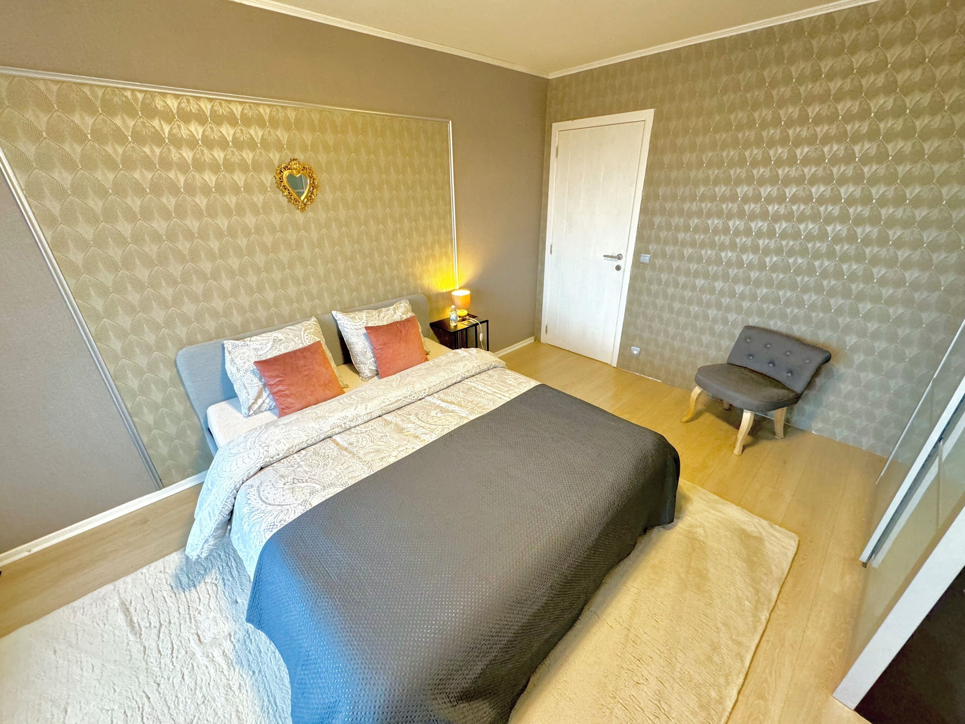 A bedroom with a large bed, a bedside table with a lamp, a chair, and a door.