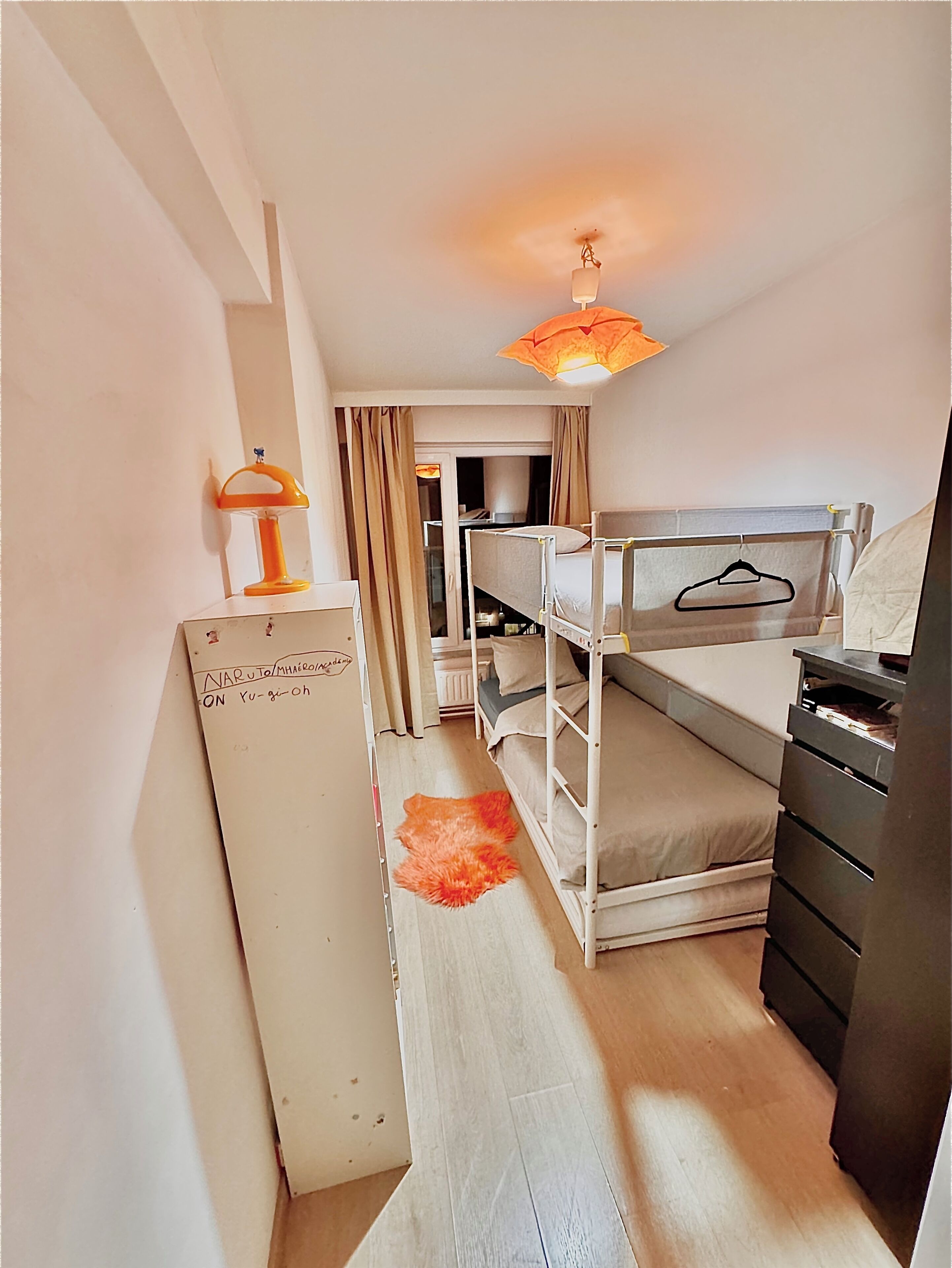 Habitación de hotel compacta con literas, un escritorio con lámpara y un armario.