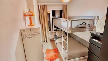 Habitación de hotel compacta con literas, un escritorio con lámpara y un armario.
