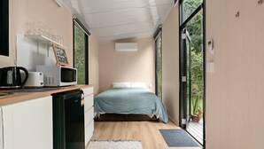 A compact room with a bed, kitchenette, and large windows. - Natural Age by Tiny Away (Bahrs Scrub)