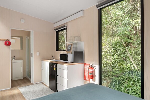 A compact kitchen with a microwave, a small refrigerator, and a window with a view of greenery.