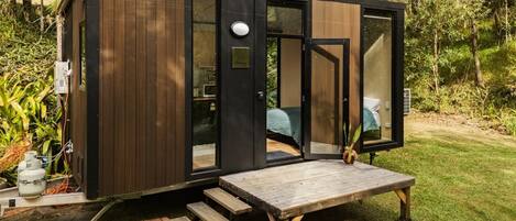 A small, modern cabin with a wooden exterior, large glass windows, and a wooden deck.