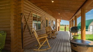 Eine Blockhütte mit einer Holzdiele, Schaukelstühlen, einem Grill und einem Whirlpool.