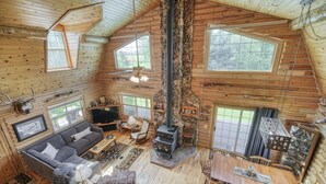 Ein rustikales Blockhaus-Interieur mit Kamin, Sofa, Esstisch und großen Fenstern.