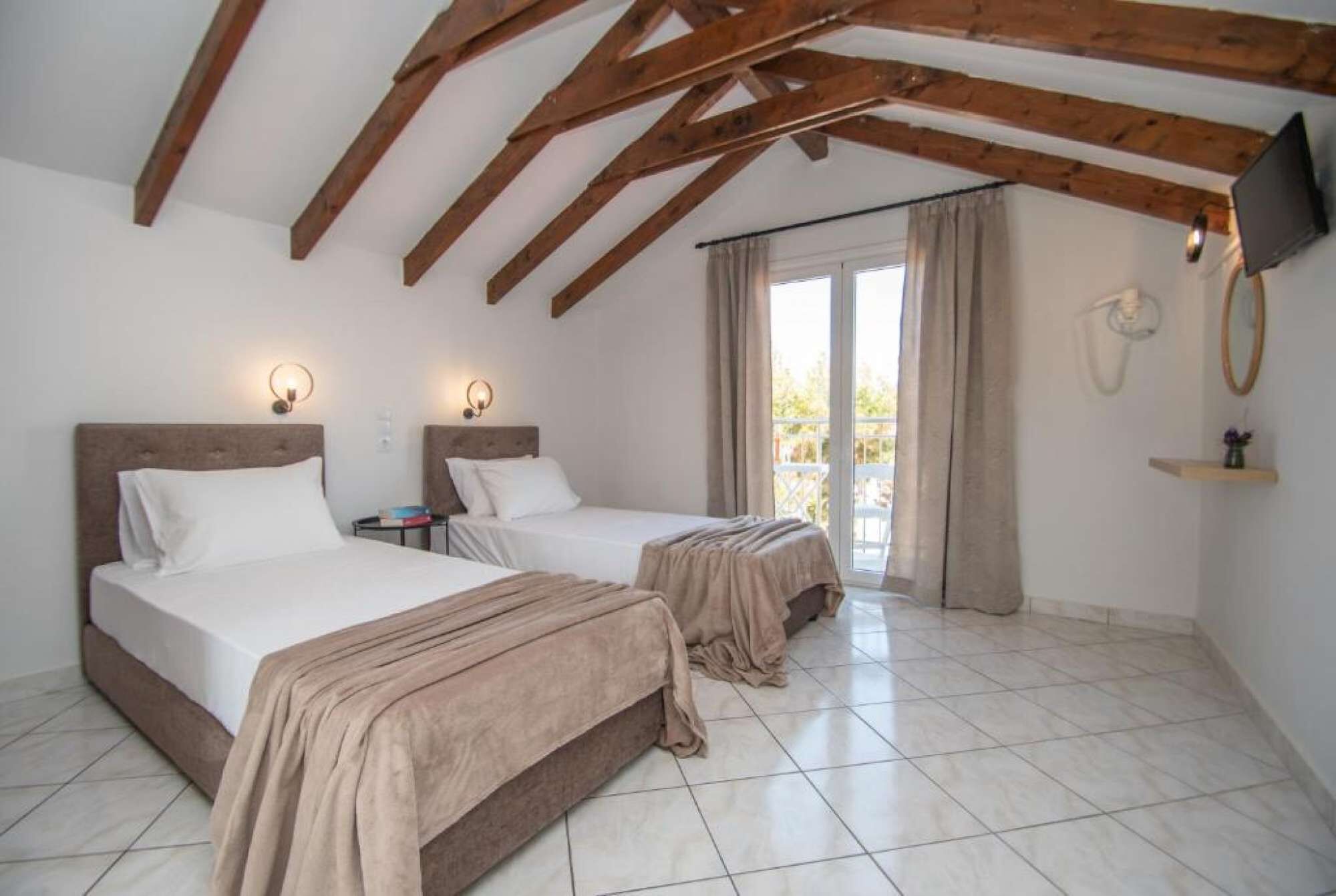 Une chambre avec deux lits, des poutres en bois au plafond, une télévision et un balcon avec des rideaux.