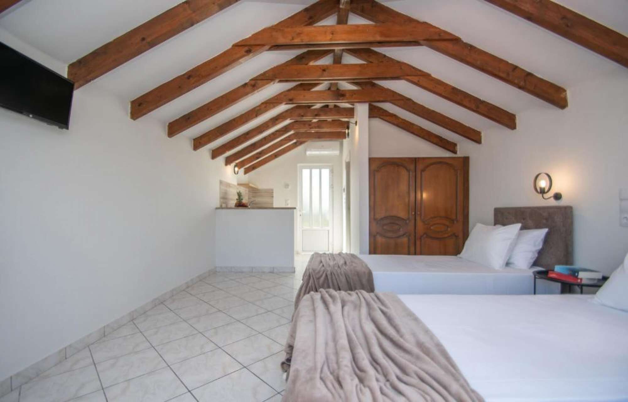 Un dormitorio con techo inclinado, una cama, un armario y una pequeña zona de kitchenette.