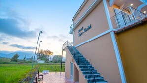 A hotel with a staircase leading to a balcony, surrounded by a landscaped garden and a view of the countryside.