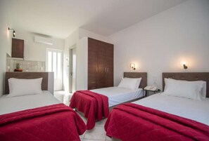 A hotel room with two beds, a wardrobe, a bedside table with a lamp, and a bathroom visible through an open door.