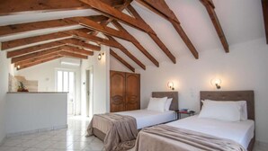 A room with two beds, wooden beams on the ceiling, a wardrobe, and a door leading to another room.