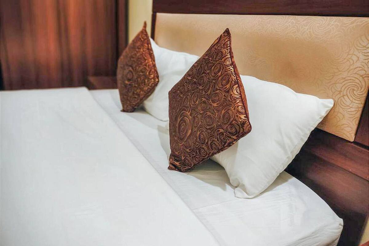 Ein ordentlich bezogenes Bett mit weißer Bettdecke und zwei dekorativen Kissen mit braunem Muster.