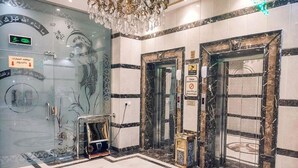 A lobby with marble flooring, a glass door with Arabic script, and two elevators with safety signs. - Al Ghubaishi Plaza (Jeddah)