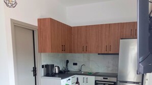 A compact kitchen with wooden cabinets, a stainless steel refrigerator, and a dining table with chairs. - KaVros Cozy Apartment with mountain views (Paralia Kourna)