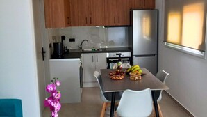 A modern kitchen with wooden cabinets, a stainless steel refrigerator, and a dining area with a marble table and chairs. - KaVros Cozy Apartment with mountain views (Paralia Kourna)