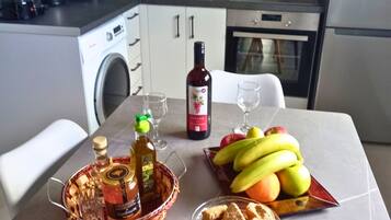 A kitchen with a washing machine, a refrigerator, and a dining table with food and drinks.