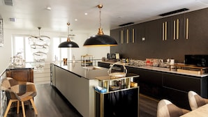 Una cocina moderna con una isla central, iluminación colgante y una zona de comedor con una silla de madera.