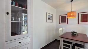 Un coin repas avec une table en bois, des chaises blanches, une suspension et des tableaux encadrés au mur.
