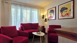Un salon avec des canapés rouges, une petite table sur laquelle est posée une plante, une cheminée et deux œuvres d’art encadrées accrochées au mur.